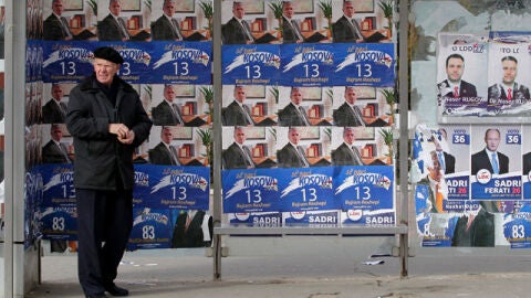  Un hombre camina frente a unos carteles electorales del Partido Democr&aacute;tico (PDK)