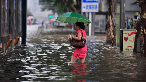 Una mujer camina por una calle inundada hacia una parada de autob&uacute;s en Wuhan