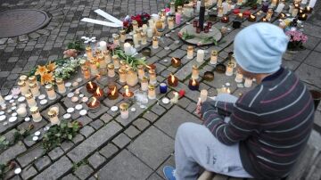 Un joven sentado en un banco junto a una multitud de velas