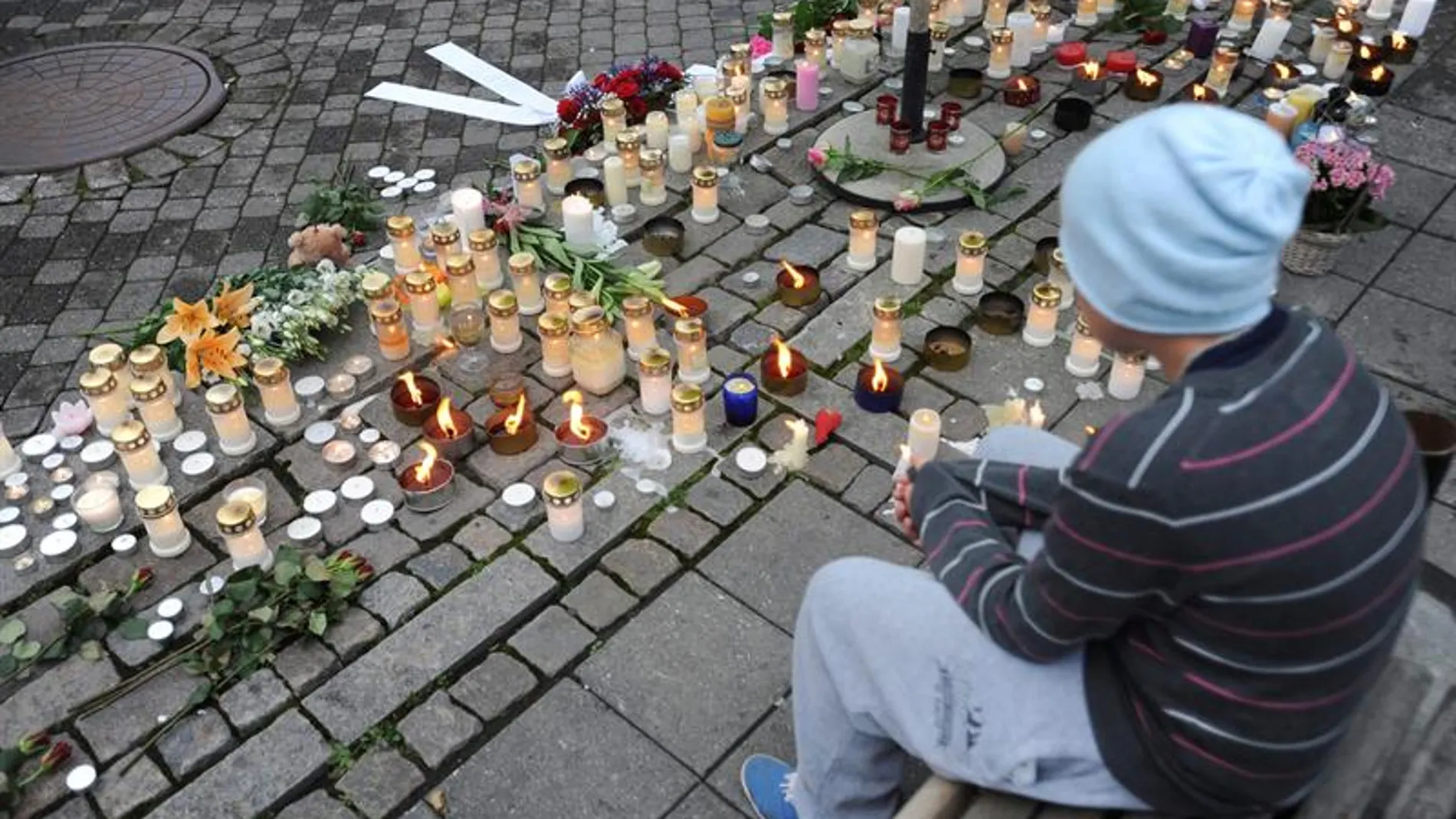 Un joven sentado en un banco junto a una multitud de velas Un joven sentado en un banco junto a una multitud de velas