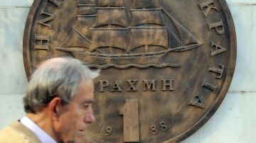 Un hombre camina frente al drachma griego 