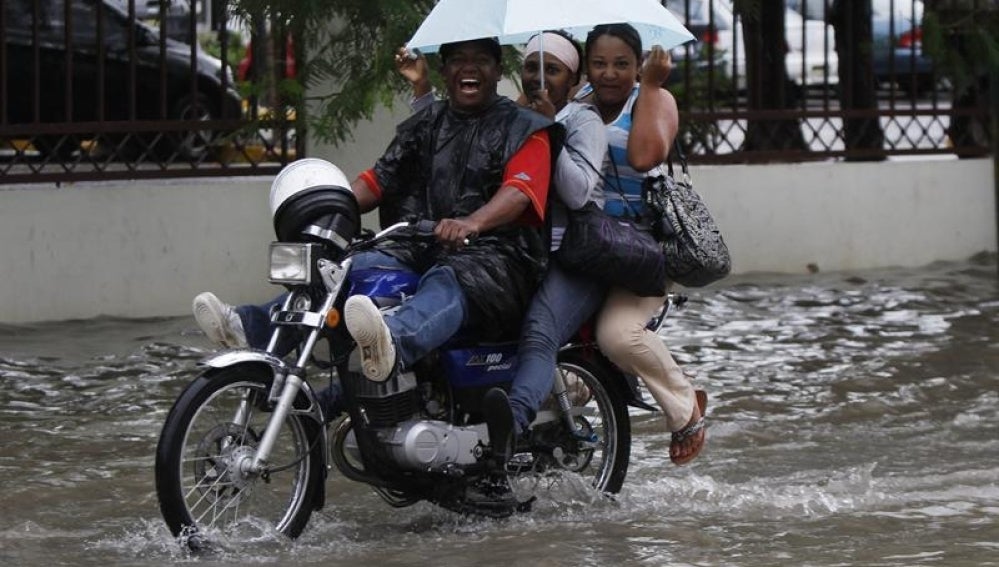 Tres personas se desplazan bajo la lluvia en Santo Domingo.