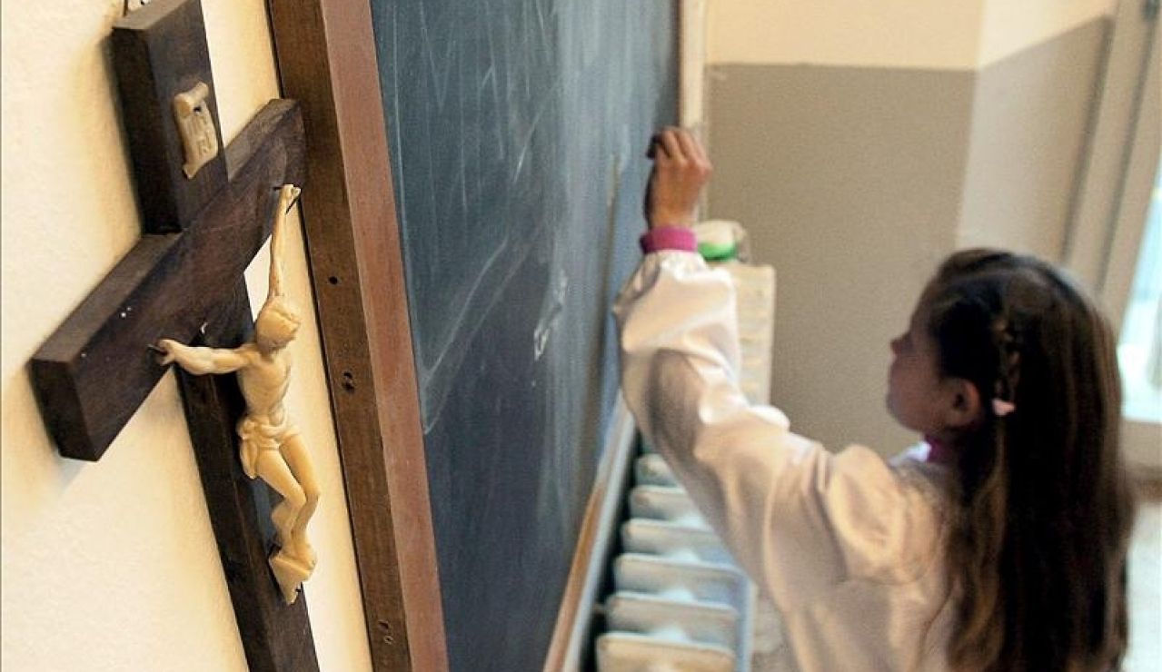 Una alumna escribe en la pizarra de una clase en la que cuelga un crucifijo