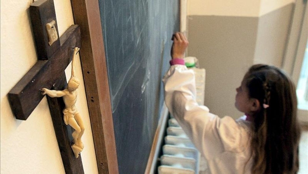 Una alumna escribe en la pizarra de una clase en la que cuelga un crucifijo