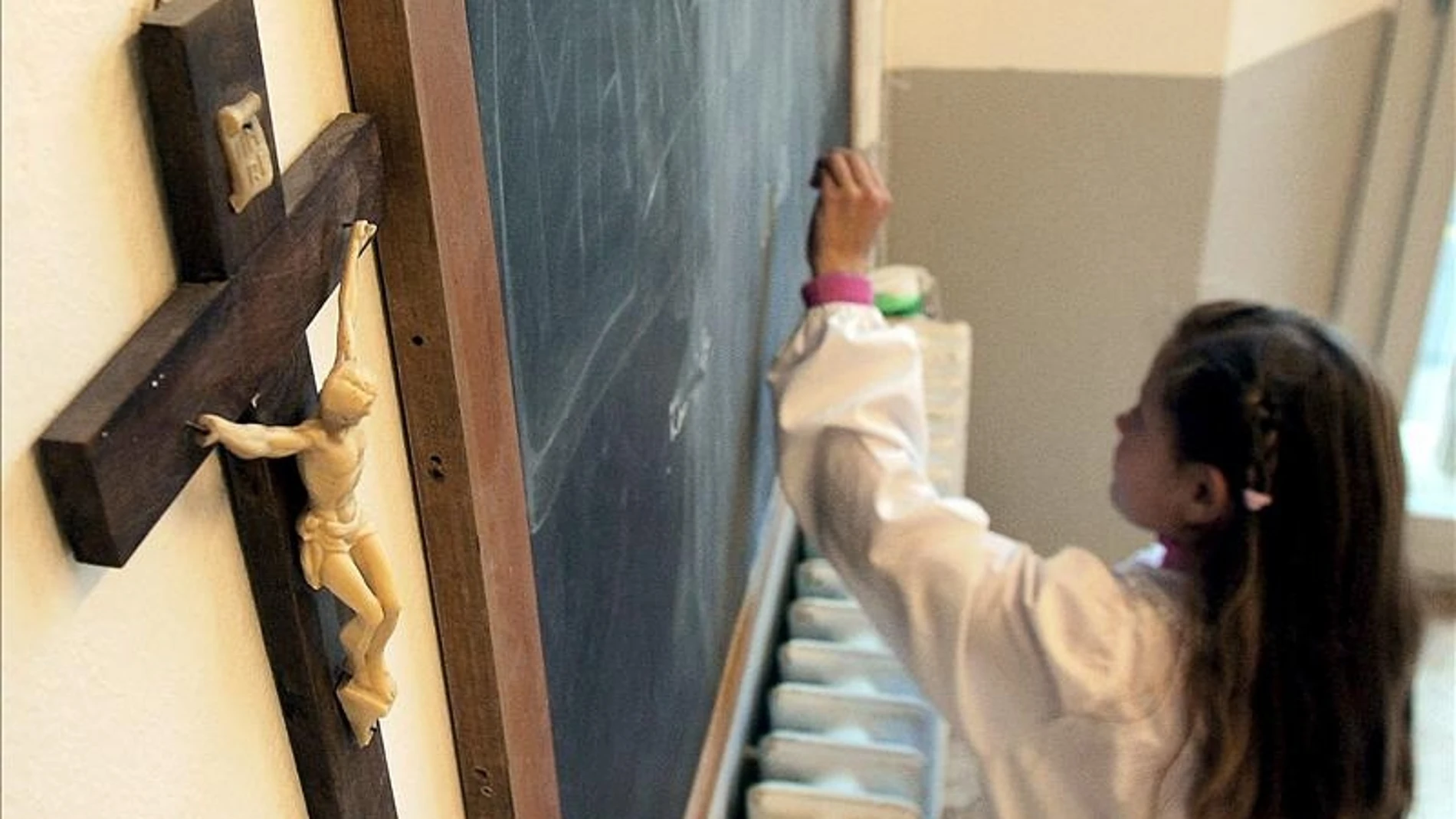 Una alumna escribe en la pizarra de una clase en la que cuelga un crucifijo Una alumna escribe en la pizarra de una clase en la que cuelga un crucifijo