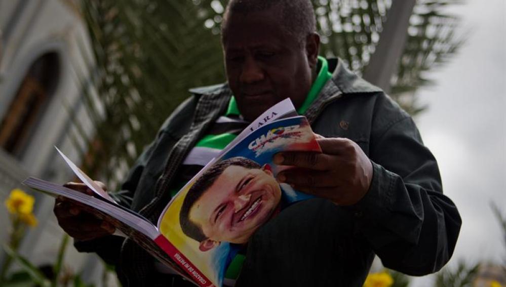 Un hombre sostiene un libro con la imagen del presidente Hugo Chávez 