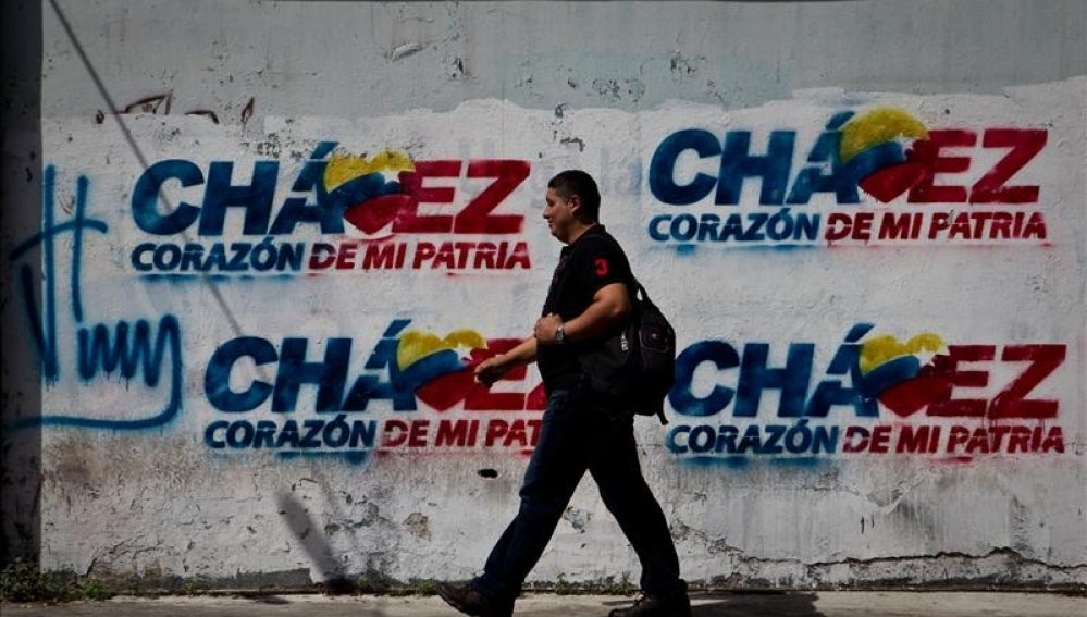  Transeúntes caminan frente a paredes decoradas con grafitis alusivos al presidente Hugo Chávez.