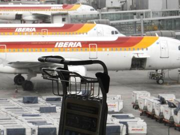 Un carrito de equipajes ante varios aviones de Iberia