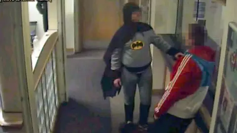 Un hombre disfrazado de Batman entrega un delincuente Un hombre disfrazado de Batman entrega un delincuente