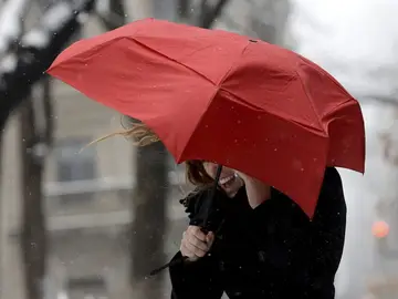 Una mujer habla por su teléfono móvil tratando de protegerse del viento Una mujer habla por su teléfono móvil tratando de protegerse del viento