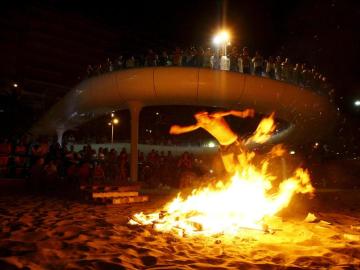 Varias personas observan una de las hogueras encendidas en una playa.