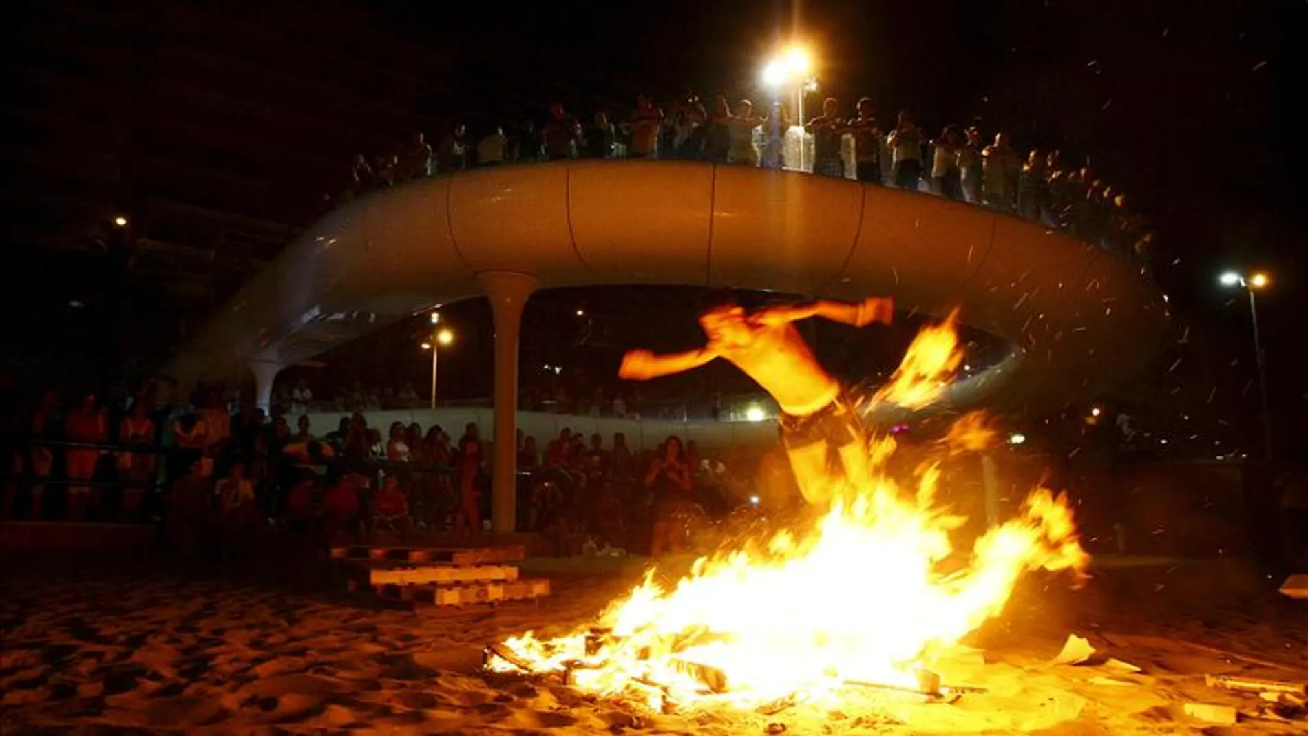 Varias personas observan una de las hogueras encendidas en una playa. Varias personas observan una de las hogueras encendidas en una playa.