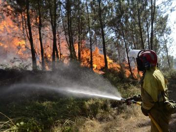 Un bombero intenta apagar una zona invadida por las llamas en A Merca