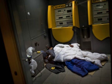 Dos vagabundos duermen en un cajero en Barcelona.