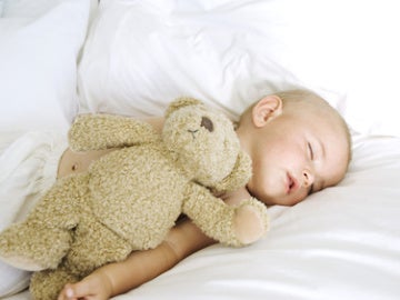 Un bebé dormido junto a un osito de peluche.