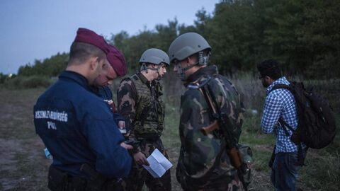 Polic&iacute;as y soldados comprueban la documentaci&oacute;n de un refugiado en la frontera entre Serbia y Hungr&iacute;a.