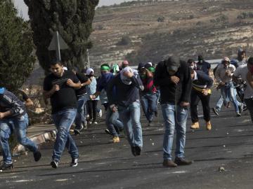 Palestinos corren para ponerse a cubierto durante un enfrentamiento con el Ejército israelí en Ramala