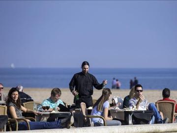 Varias personas disfrutan de las temperaturas suaves tomando un aperitivo en una terraza