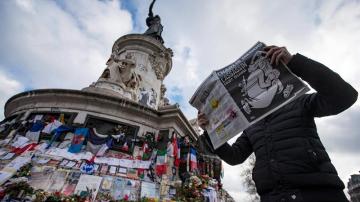 Un hombre lee la revista Charlie Hebdo frente al homenaje a las víctimas