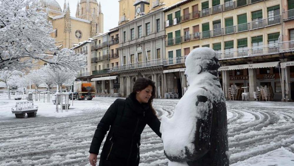 Una mujer retira la nieve sobre la escultura del poeta Antonio Machado, en la Plaza Mayor de Segovia