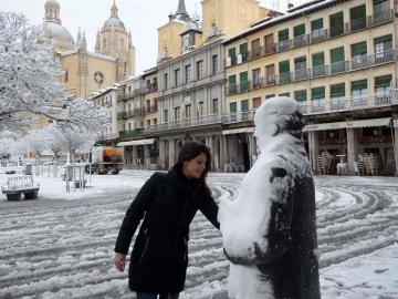 Una mujer retira la nieve sobre la escultura del poeta Antonio Machado, en la Plaza Mayor de Segovia