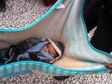 Un bebe descansa en una manta mientras refugiados esperan subir a bordo de un tren en Macedonia