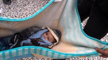 Un bebe descansa en una manta mientras refugiados esperan subir a bordo de un tren en Macedonia