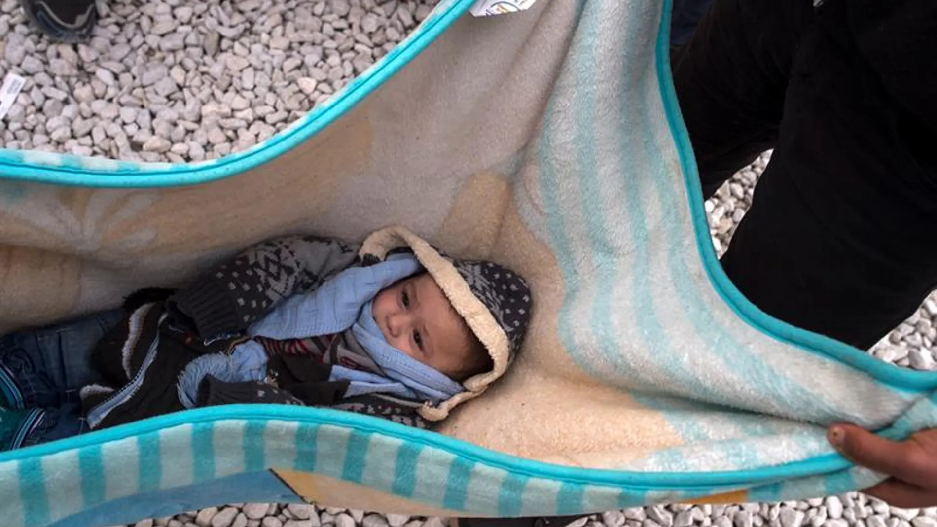 Un bebe descansa en una manta mientras refugiados esperan subir a bordo de un tren en Macedonia Un bebe descansa en una manta mientras refugiados esperan subir a bordo de un tren en Macedonia