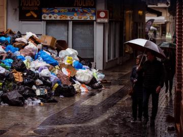 Varias personas caminan por una calle del centro de Málaga junto a la basura acumulada