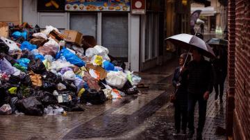 Varias personas caminan por una calle del centro de Málaga junto a la basura acumulada