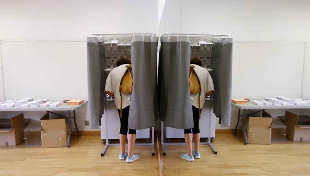 Un elector con su imagen reflejada en un espejo elige su papeleta para ejercer su derecho al voto en el Centro Cultural Volturno, en la localidad madrileña de Pozuelo de Alarcón.