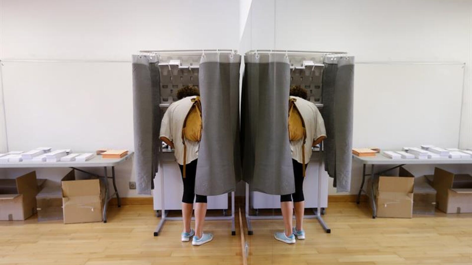 Un elector con su imagen reflejada en un espejo elige su papeleta para ejercer su derecho al voto en el Centro Cultural Volturno, en la localidad madrile&ntilde;a de Pozuelo de Alarc&oacute;n.