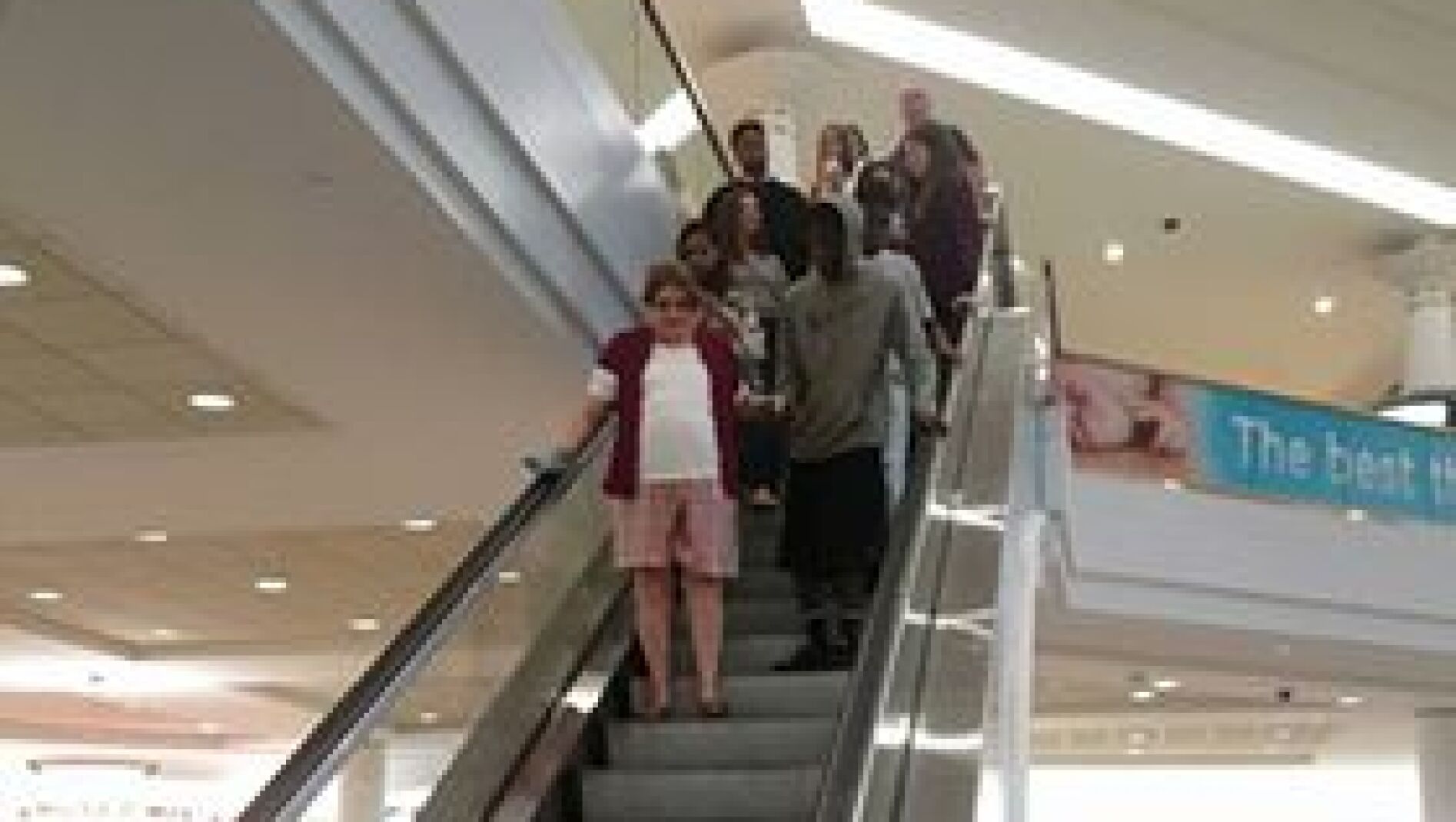 Joven ayudando a una anciana a bajar las escaleras mec&aacute;nicas