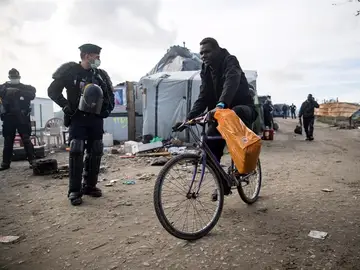 Agentes de policía galos observan a varios migrantes que son evacuados del campamento de Calais Agentes de policía galos observan a varios migrantes que son evacuados del campamento de Calais