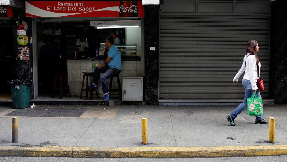 Un comercio abierto al lado de otro con las persianas cerradas