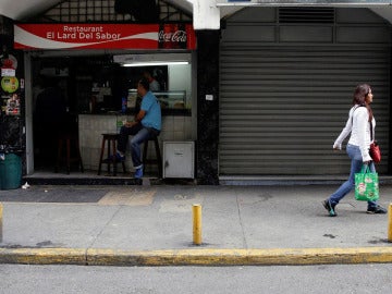 Un comercio abierto al lado de otro con las persianas cerradas