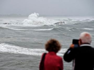 Unos vecinos toman imágenes en una playa afectada por un fuerte temporal.