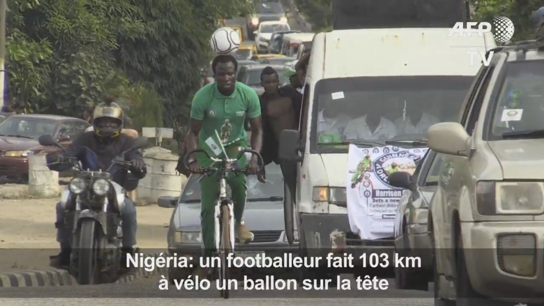 Harrison Chinedu montado en bici con el bal&oacute;n en la cabeza
