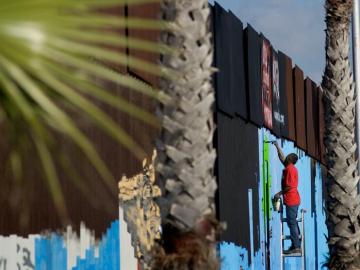 Un voluntario pinta murales en la cerca que marca el límite en la frontera entre EEUU y México