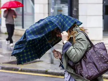 Una mujer intenta sujetar el paraguas que le protege de la lluvia debido al fuerte viento Una mujer intenta sujetar el paraguas que le protege de la lluvia debido al fuerte viento