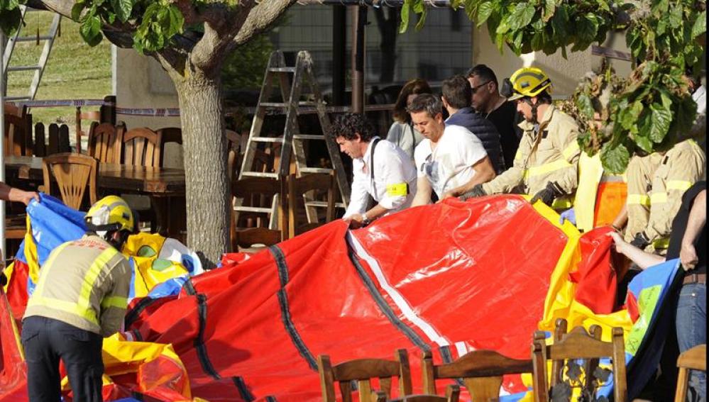 Varios operarios y bomberos retiran el castillo hinchable del restaurante Mas Oller