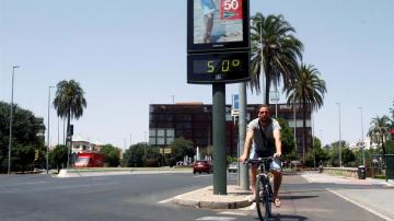Un joven pasa con su bicicleta junto a un termómetro que marca 50 grados en una calle de Córdoba