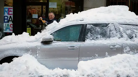 Un hombre retira la capa de nieve de un coche Un hombre retira la capa de nieve de un coche