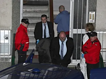 Miembros de los servicios funerarios con el cuerpo de uno de los miembros del matrimonio Miembros de los servicios funerarios con el cuerpo de uno de los miembros del matrimonio