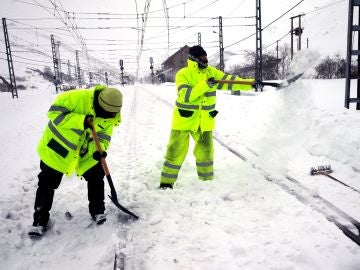 Dos operarios retiran la nieve en la estación de ferrocarril de Busdongo