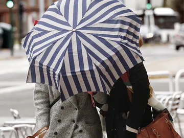 Dos mujeres se protegen con un paragüas de la lluvia y el viento Dos mujeres se protegen con un paragüas de la lluvia y el viento
