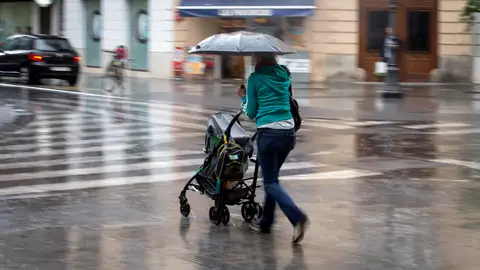 Una mujer con un carrito se protege con un paraguas de la lluvia Una mujer con un carrito se protege con un paraguas de la lluvia