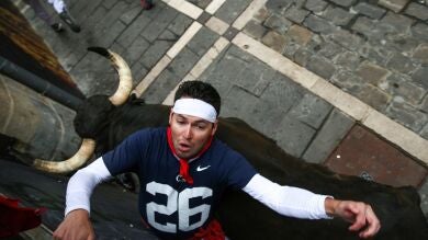 Los dos momentos de mayor peligro del séptimo encierro de San Fermín: una cornada y un fuerte golpe contra la valla