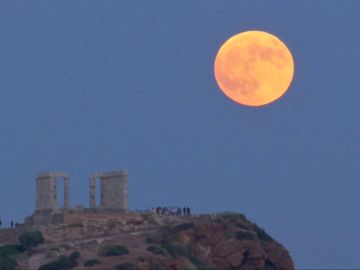 Una luna llena se levanta durante un eclipse lunar detrás de la estatua de la antigua diosa Atenea en Atenas Una luna llena se levanta durante un eclipse lunar detrás de la estatua de la antigua diosa Atenea en Atenas