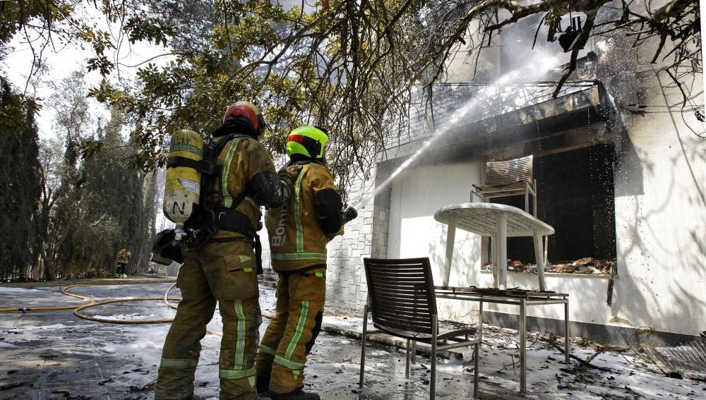 Dos bomberos refrescan el interior de una de las viviendas afectadas por el incendio forestal de Llutxent